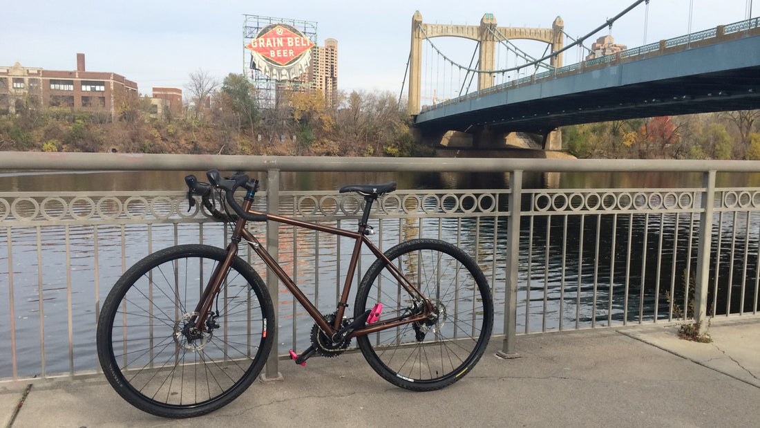 A bike sits against a railing overlooking the river. Large signs and bridges in the background.